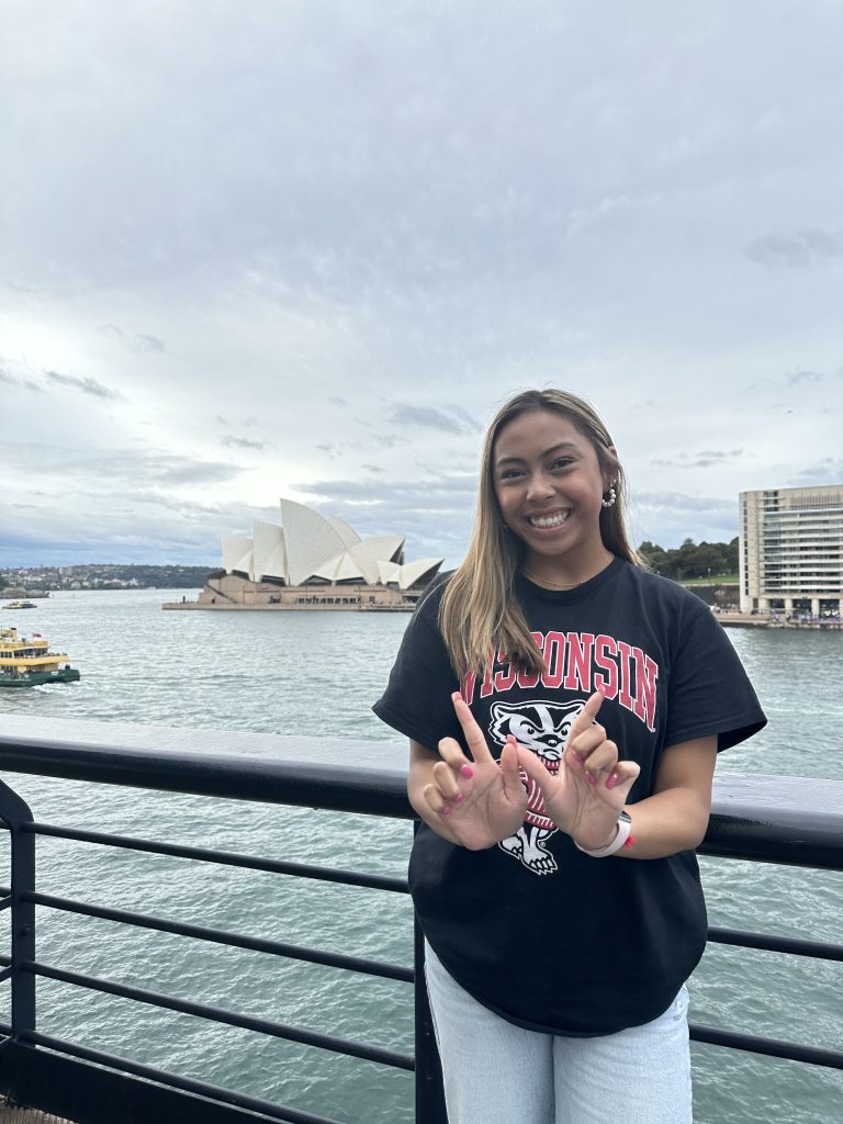UW-Madison student making the Wisconsin “W” with her hands while standing in front of the Sydney Opera House. 