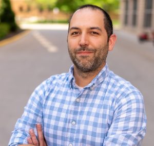 person posing in checkered shirt outdoors with arms crossed