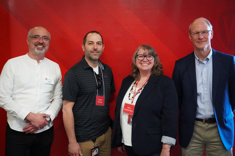 four people pose smiling against a red background