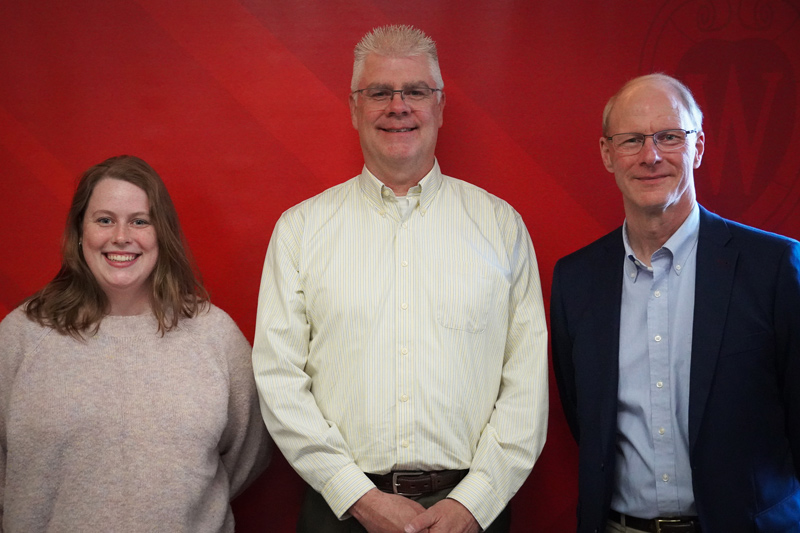 three people stand posing and smiling in front of red background