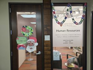 *Santa cutout, paper wreath, signage, and paper chain decorate the door and window of Human Resources office* 