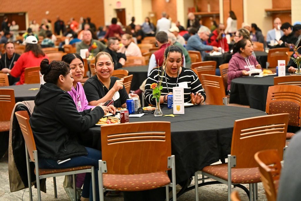 Four people sit at a round banquet table with black tablecloth, smiling and talking with varied facial expressions