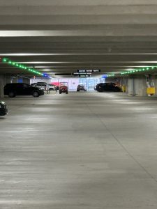 Photo of a parking garage drive lane with green lights lights above empty parking spaces.