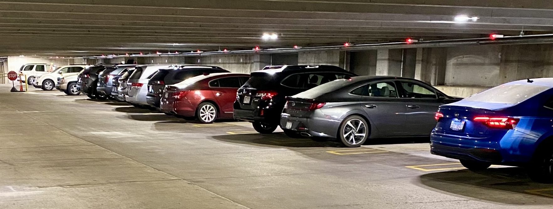 Photo of several vehicles parked in a parking garage with a red light above each vehicle.