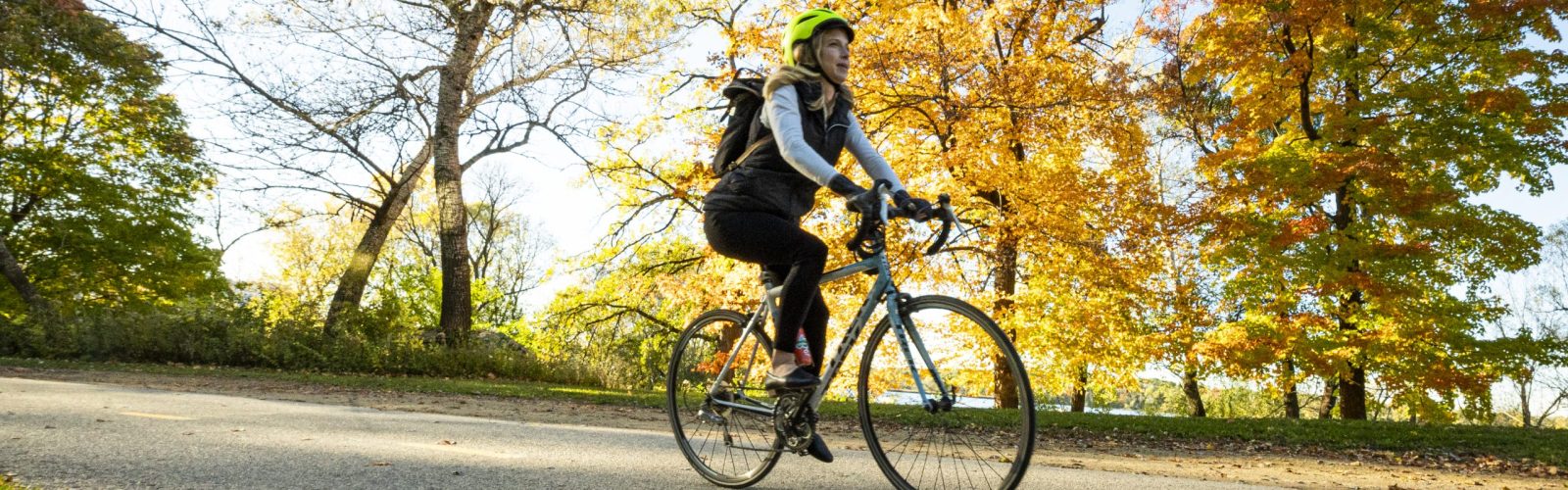 Photo of a female-presenting person riding a bicycle on a path on an autumn day.
