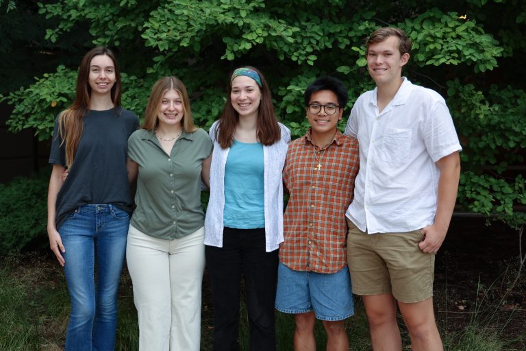 5 students standing in front of green bushes