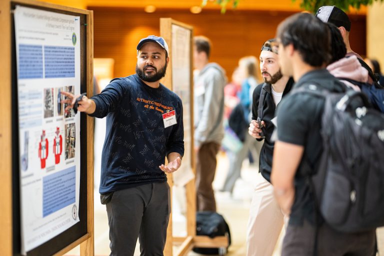 Saurabh Gupta stands in front of a research poster in a room full of people, pointing and discussing his work with attendees.