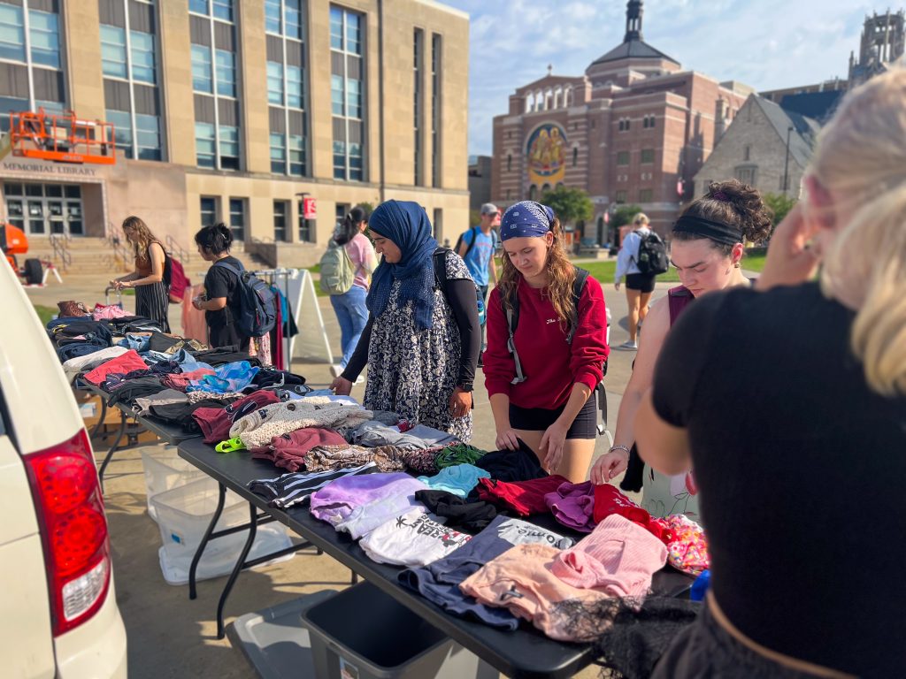 Students stand outside, sorting through stacks of clothes folded on a table