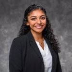 Veronica Goveas in a black jacket and white shirt in front of a gray background