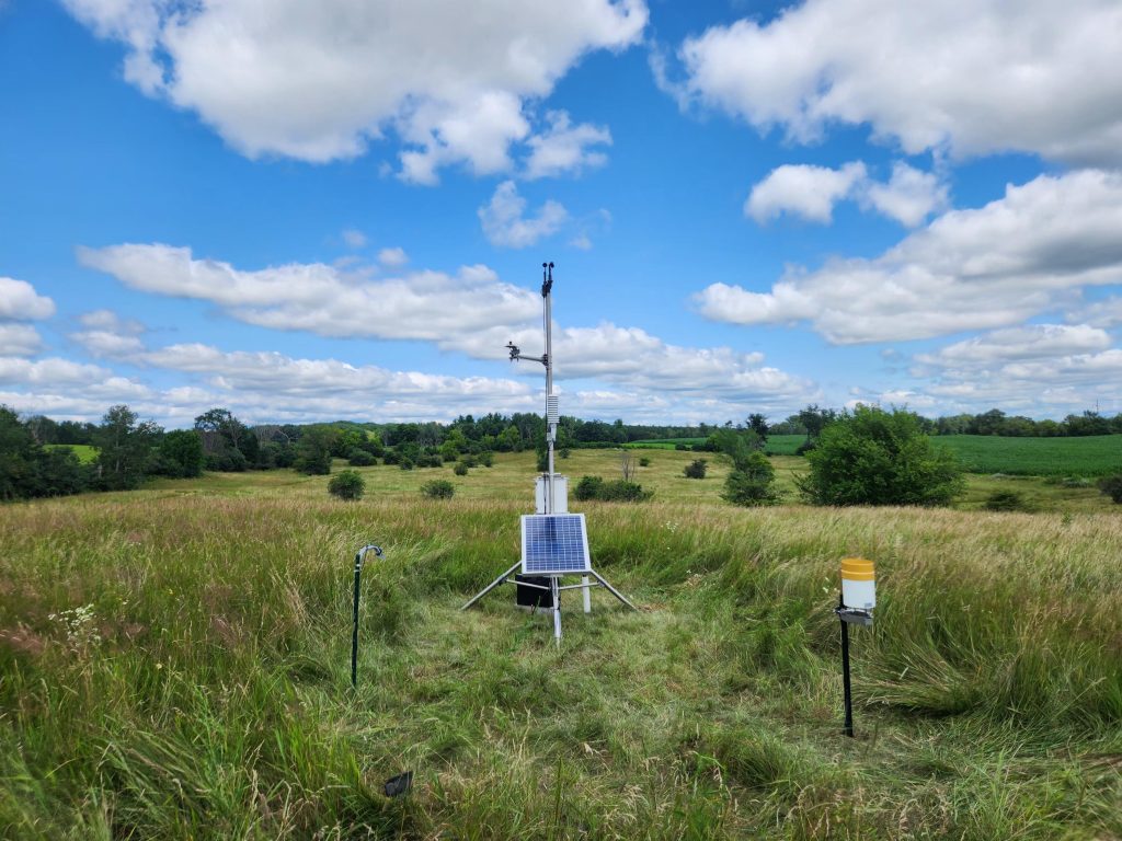 a wisconet station is in a green field against a blue sky with scattered clouds
