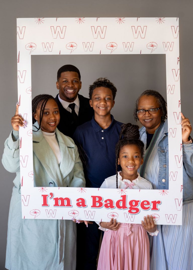 Returning adult student and family holding a frame that reads, "I'm a Badger."