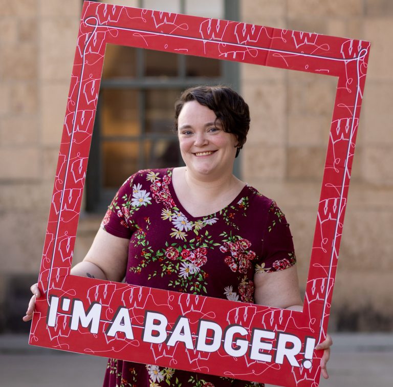 Returning adult student looking through a frame that reads, "I'm a Badger!"