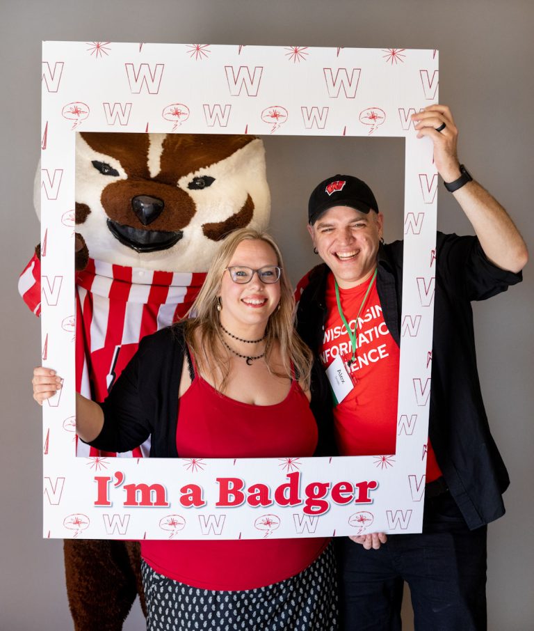 Returning adult student, spouse, and Bucky Badger all looking through a frame with the words, "I'm a Badger."