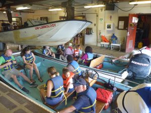 Photo taken inside Hasler Lab boat slip during Open House. Several Open House participants are sitting in the two john boats, wearing life jackets, waiting to go on boat ride.