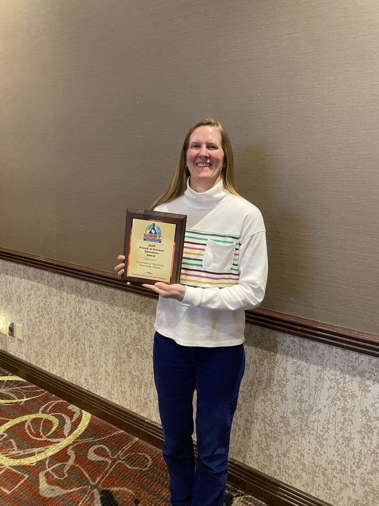 Carol warden is looking at the camera and smiling and holding the award plaque