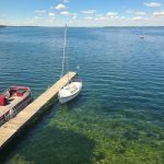 photo taken from above Hasler Lab dock showing clear water phase of Lake Mendota. Blue sky day with calm water and CFL pontoon boat on one side of dock and sail boat on other side of dock.