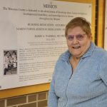 Kay Emerson stands in front of her photo with Harry Waisman