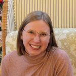 Young light brown-haired white woman smiling with metal glasses and short, light brown hair. She is wearing a pink top.