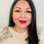 Photo of a hispanic woman with long dark hair. Wearing a cream top. Bright pink lipstick.