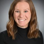 Photo of a young woman with shoulder-length brown hair. Wearing a black turtleneck.