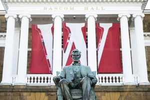 The Abraham Lincoln statue sits before Bascom Hall on Bascom Hill at the University of Wisconsin-Madison during spring on April 2, 2025. A three-paneled W banner hangs between the building’s columns. (Photo by Jeff Miller / UW–Madison)