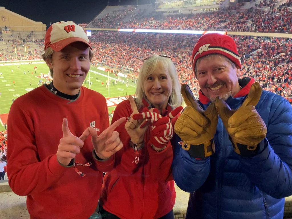 Will, Susan, and Bill Kirkpatrick using their fingers to form W's at a Badger football game