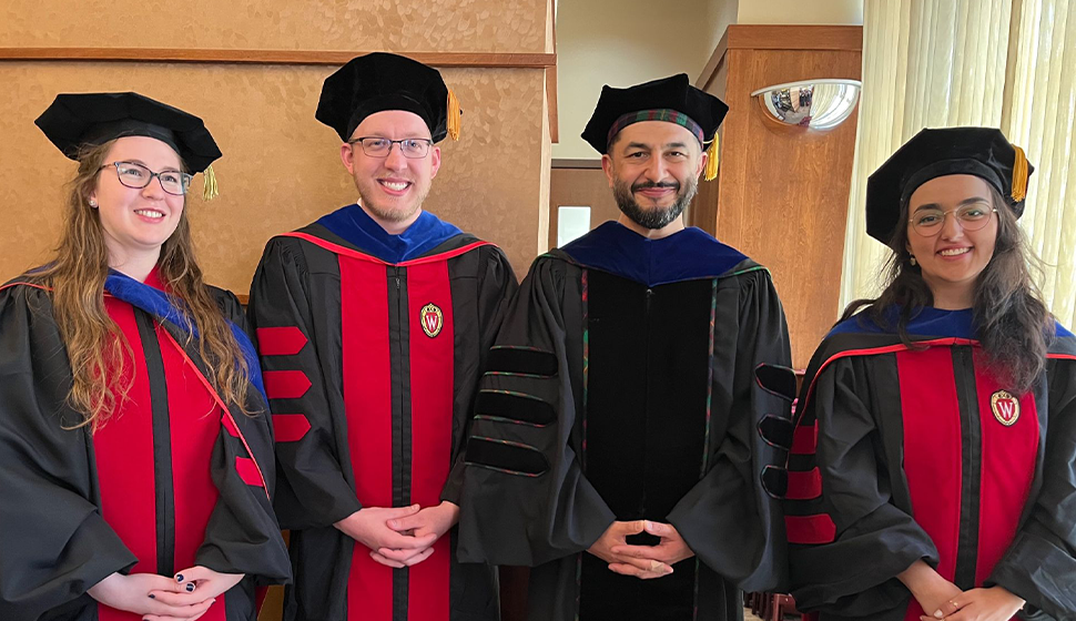 Three PhD students in caps and gowns with Professor Bilge Mutlu.